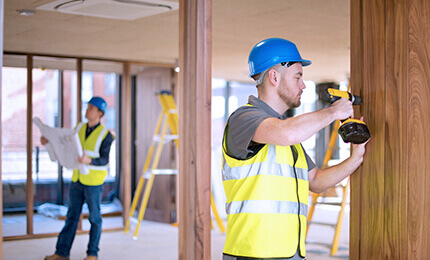 A construction worker with a drill and another with a construction project