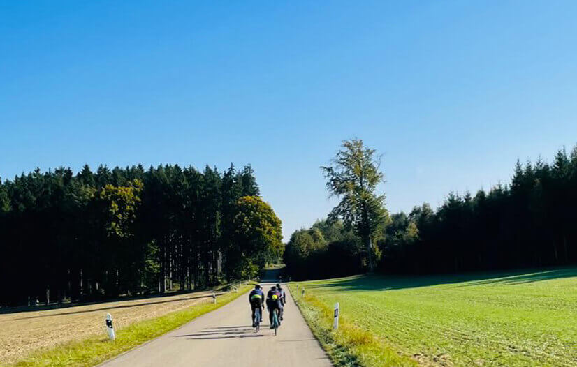 Three cyclists riding an asphalt road through the fields