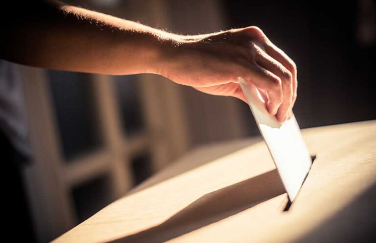 an image of a person putting a voting ballot into a ballot collection box